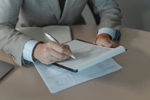 Person in a suit holding a pen over a document on a clipboard